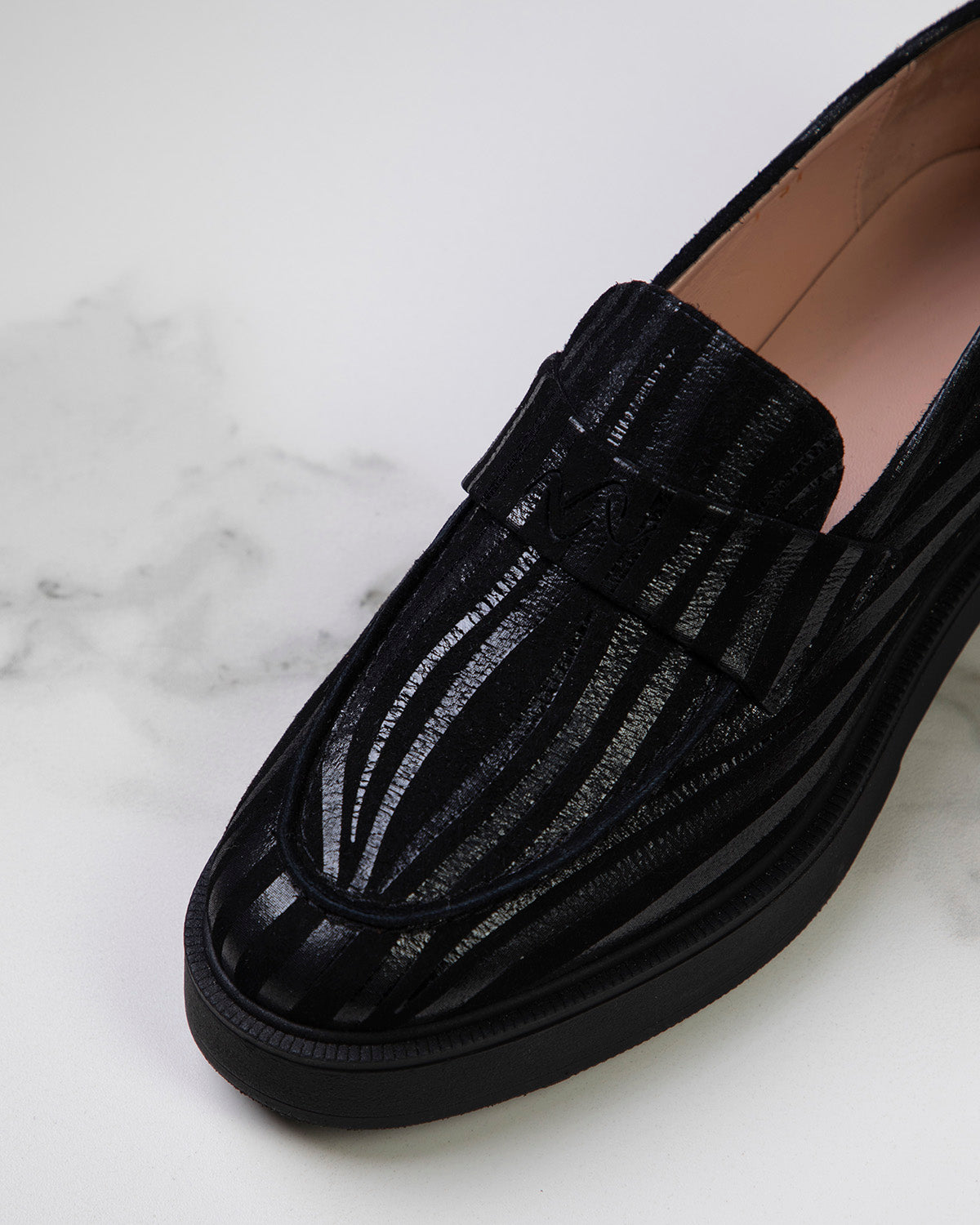 Gros plan sur le grain fin et la texture soyeuse du cuir caprin noir, soulignant la qualité artisanale du mocassin.