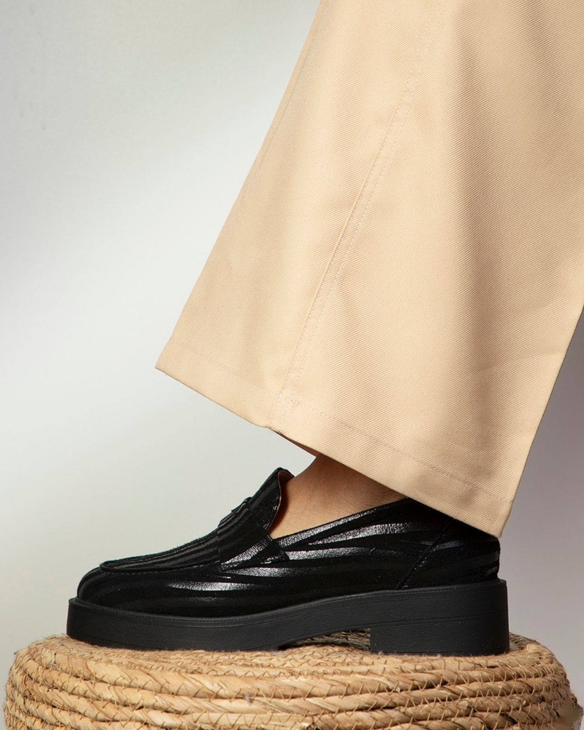 Profil d'un mocassin noir en cuir porté sur un tabouret, montrant l'ajustement du chaussant adapté aux différentes largeurs de pieds