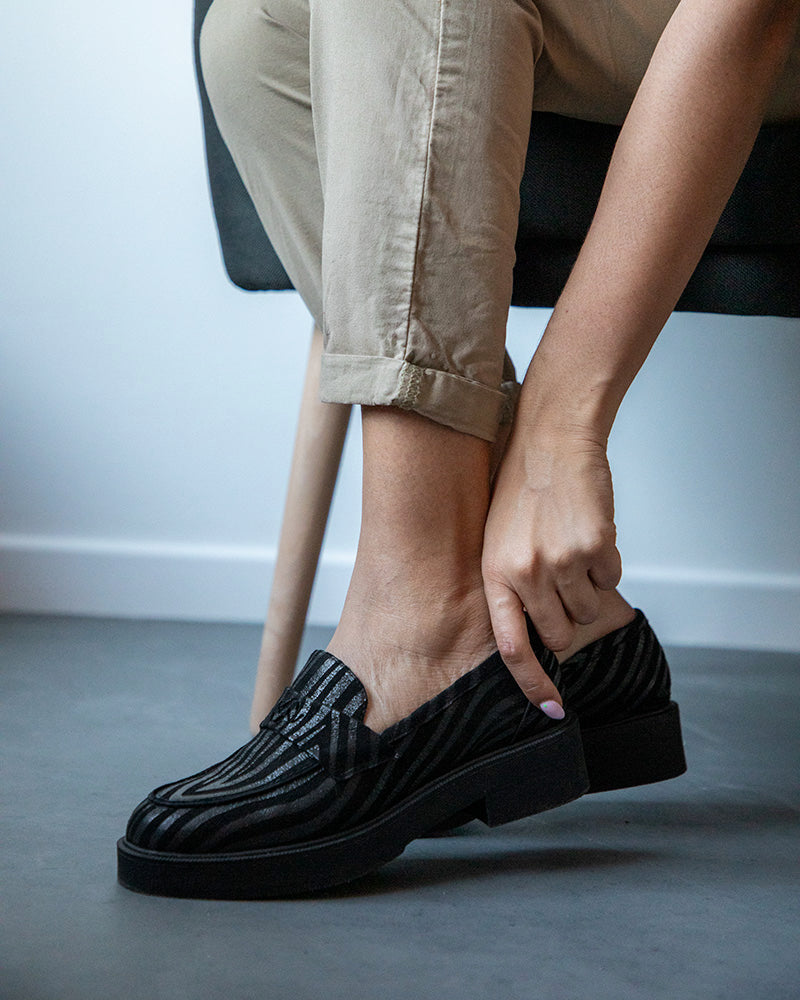 Mocassins à bout amande en cuir caprin noir, reconnus pour leur souplesse, portés par une personne assise